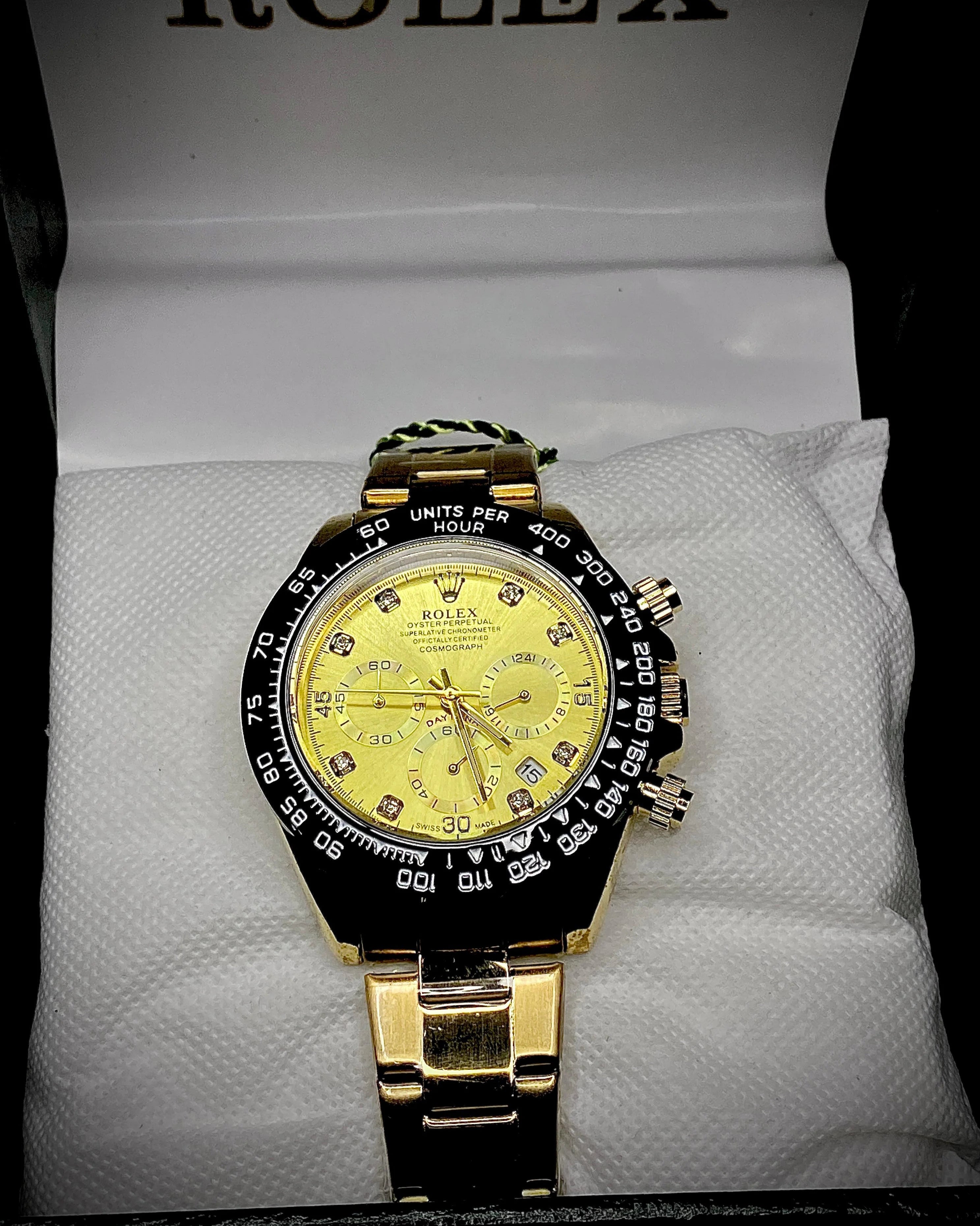 Gold and black Rolex watch on a white cushion with 'Rolex' branding in the background.